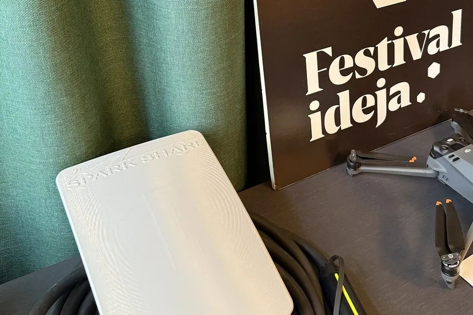 White SparkShare BOXEV with a coiled Type 2 cable in front of a Festival of Ideas sign